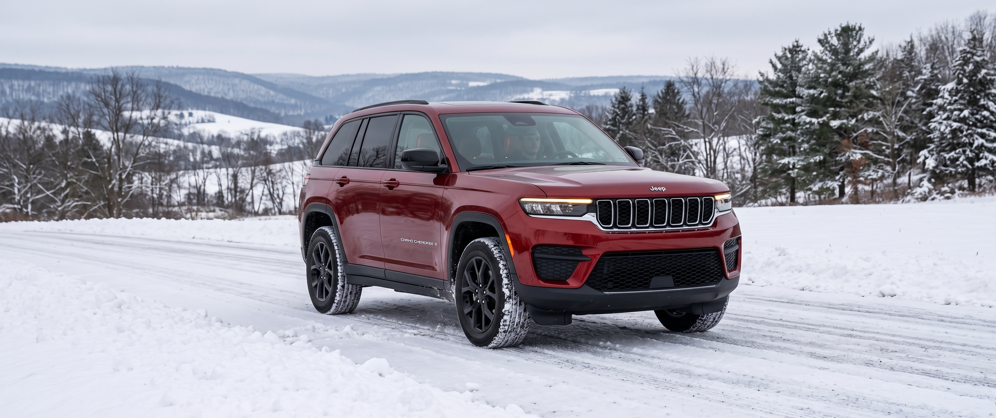 Red Jeep Grand Cherokee driving on a snow-covered road surrounded by winter scenery and trees.
