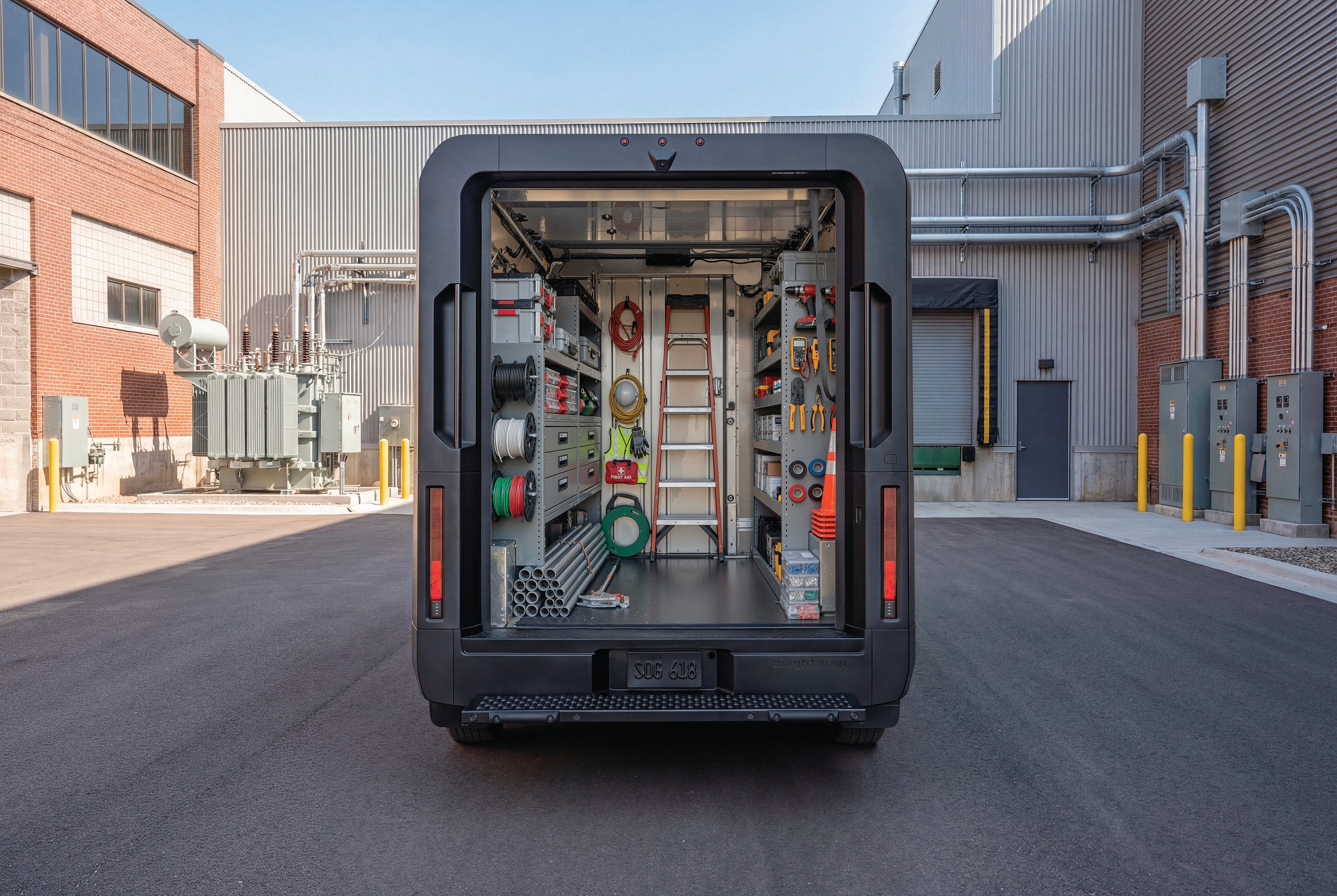Open back of a black BrightDrop electric service van loaded with organized tools and equipment outside a building.