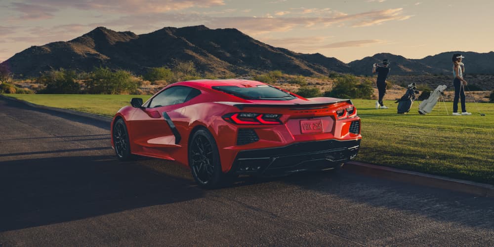 Red Chevrolet Corvette C8 parked next to a golf course at sunset with mountains in the background.