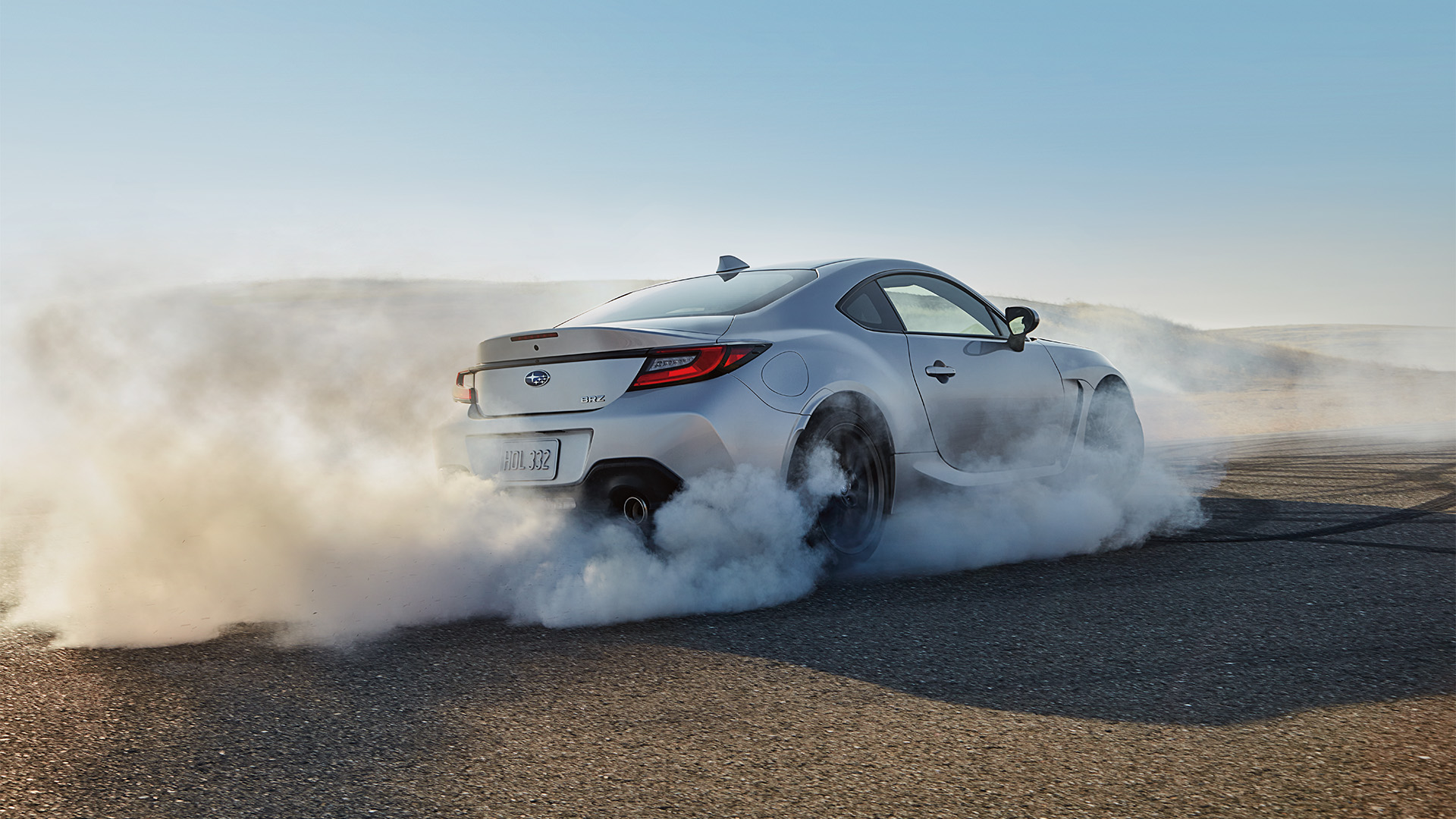 Silver Subaru BRZ sports car doing a burnout on an asphalt track surrounded by thick white tire smoke.