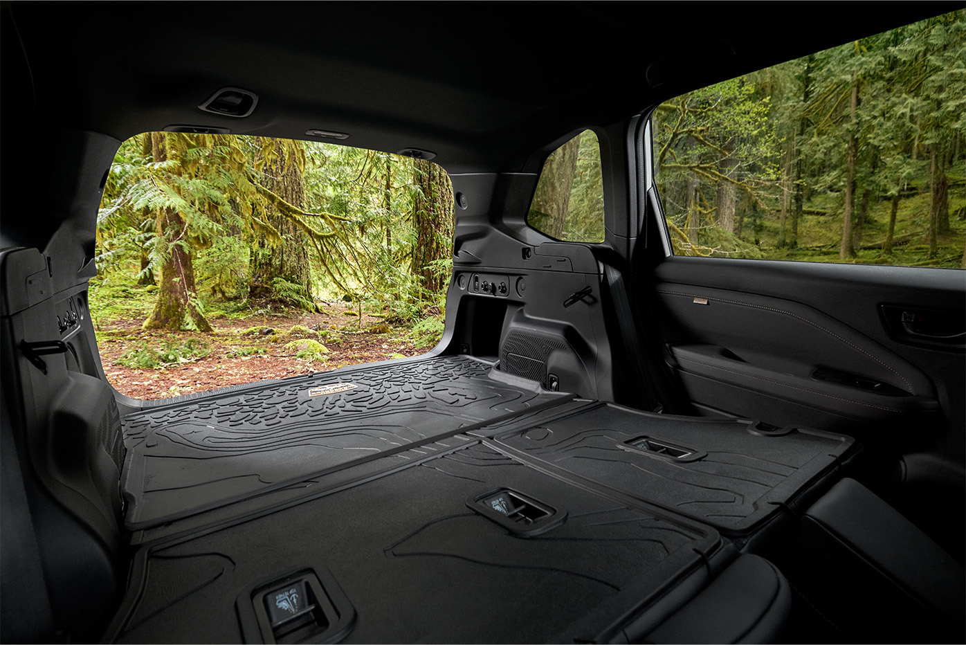 Spacious SUV cargo area with folded seats and protective rubber mats looking out into a green forest.