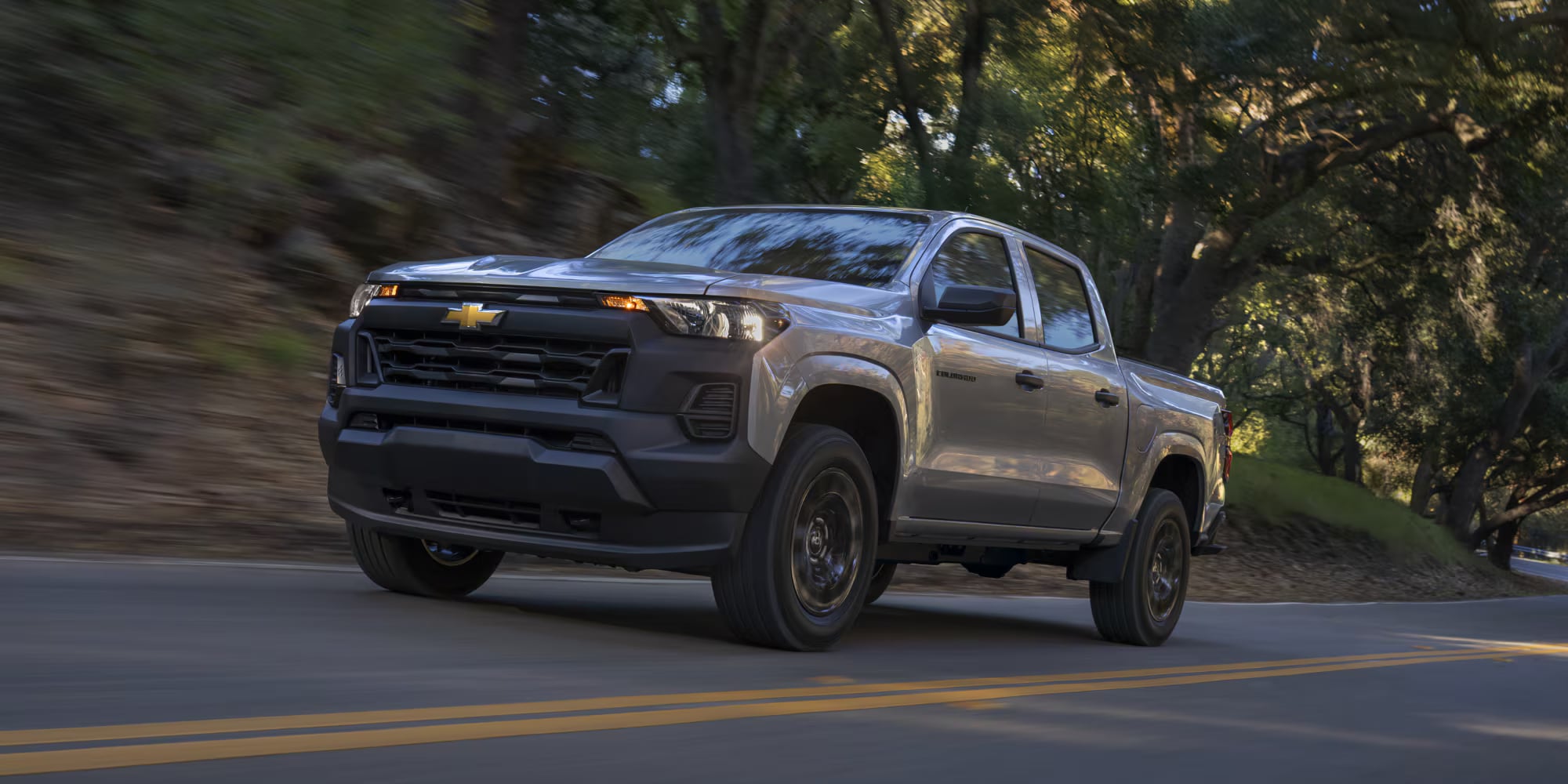 Silver Chevrolet Colorado driving along a tree-lined road