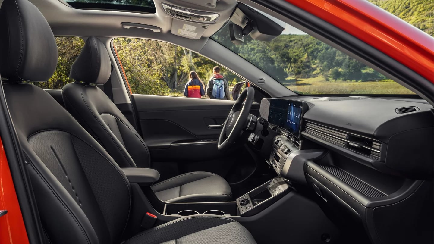 Interior view of a modern vehicle with black leather seats, digital screen, and two hikers visible outside.