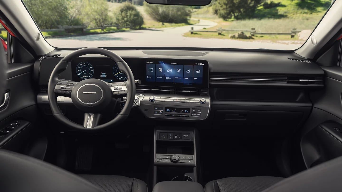 Front cabin view of a modern car interior showing the steering wheel, digital dashboard displays, and center console.