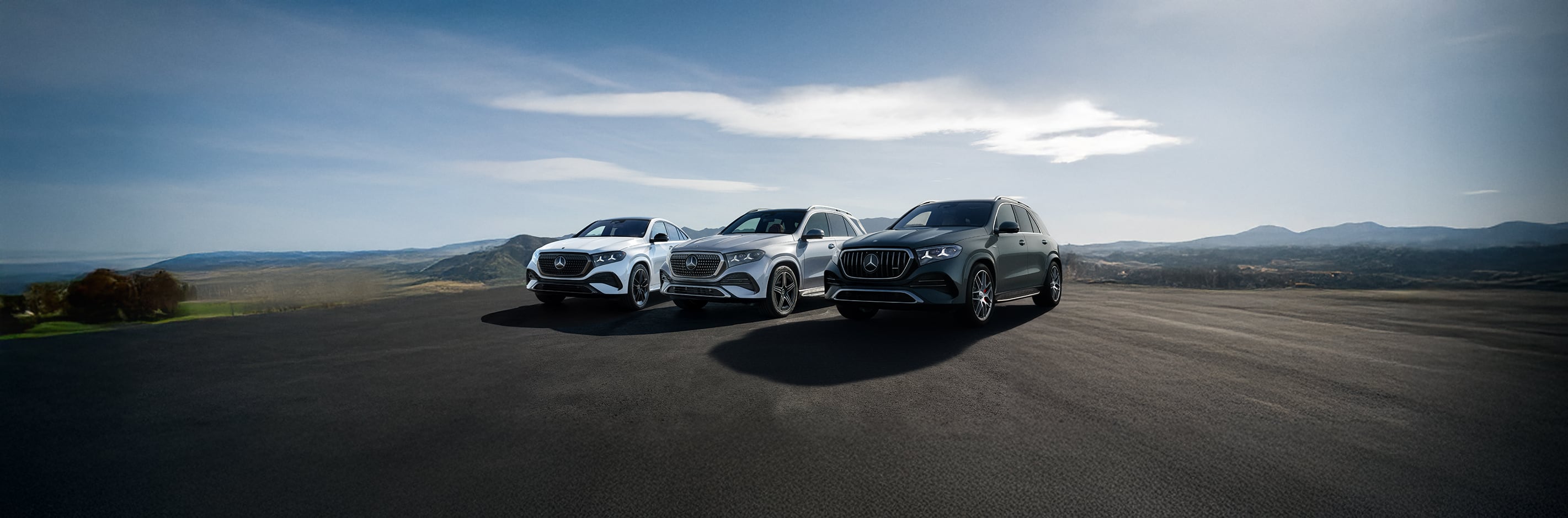 Three Mercedes-Benz luxury SUVs parked overlooking scenic mountains.