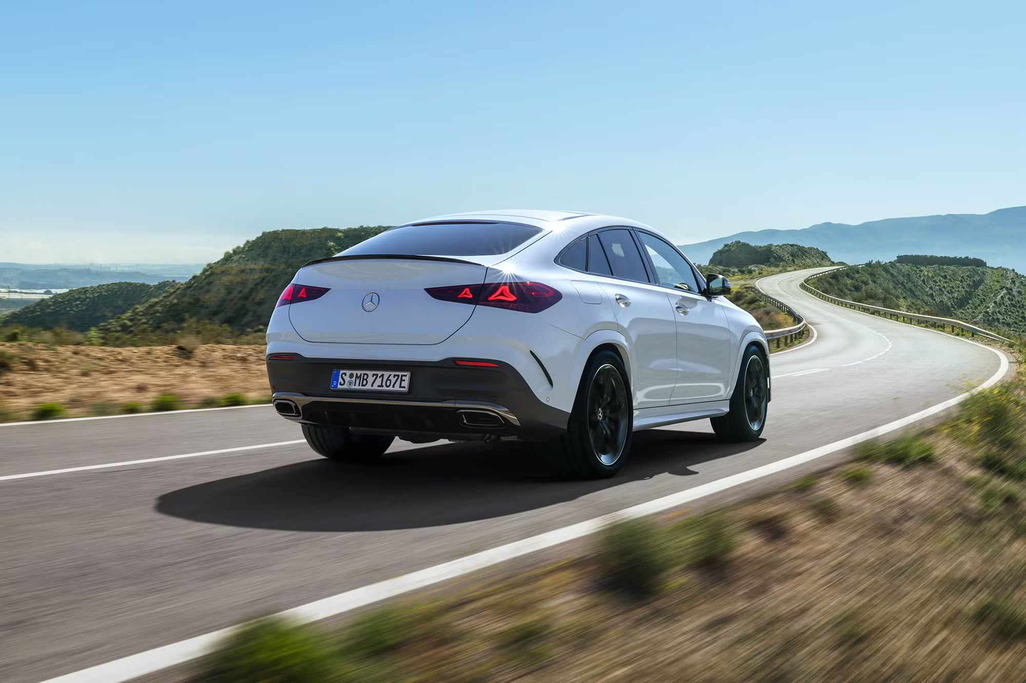 White Mercedes-Benz SUV driving along a scenic mountain road.