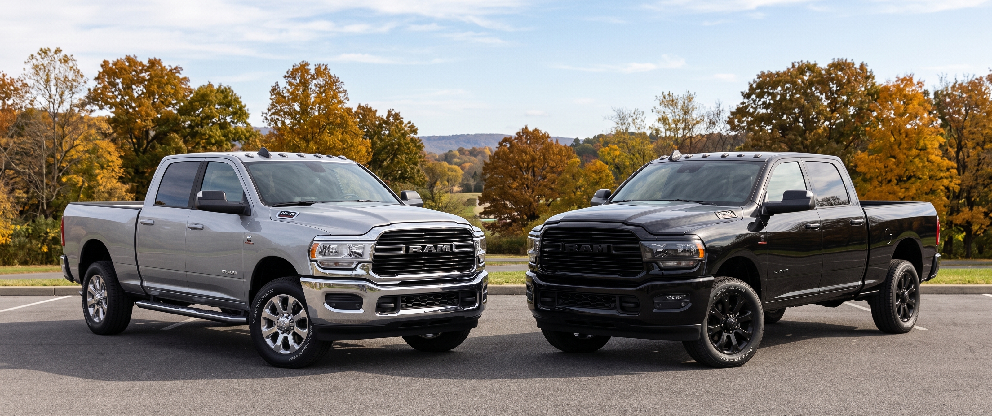 Silver Ram heavy-duty pickup truck parked next to an all-black Ram truck against an autumn treeline background.