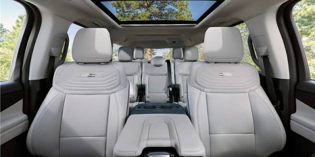 Interior view of a luxury vehicle showing three rows of light gray leather seating and a panoramic sunroof.