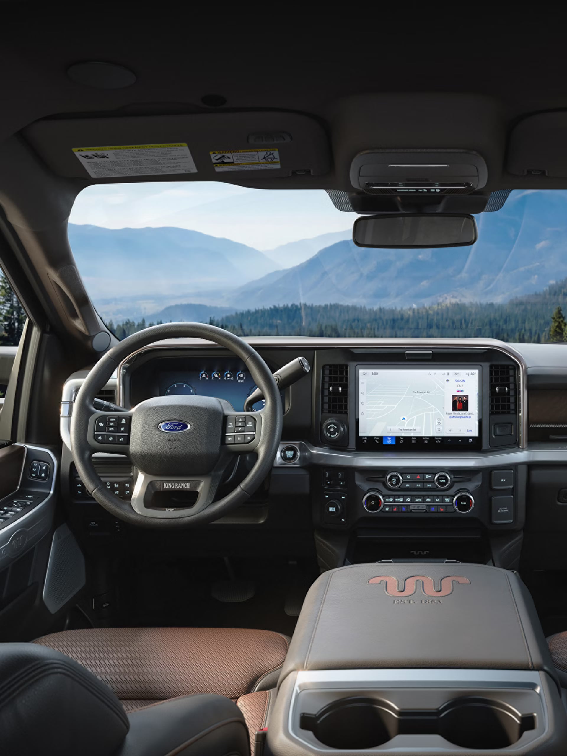 Interior view of a Ford King Ranch truck dashboard looking out towards scenic pine trees and mountains.