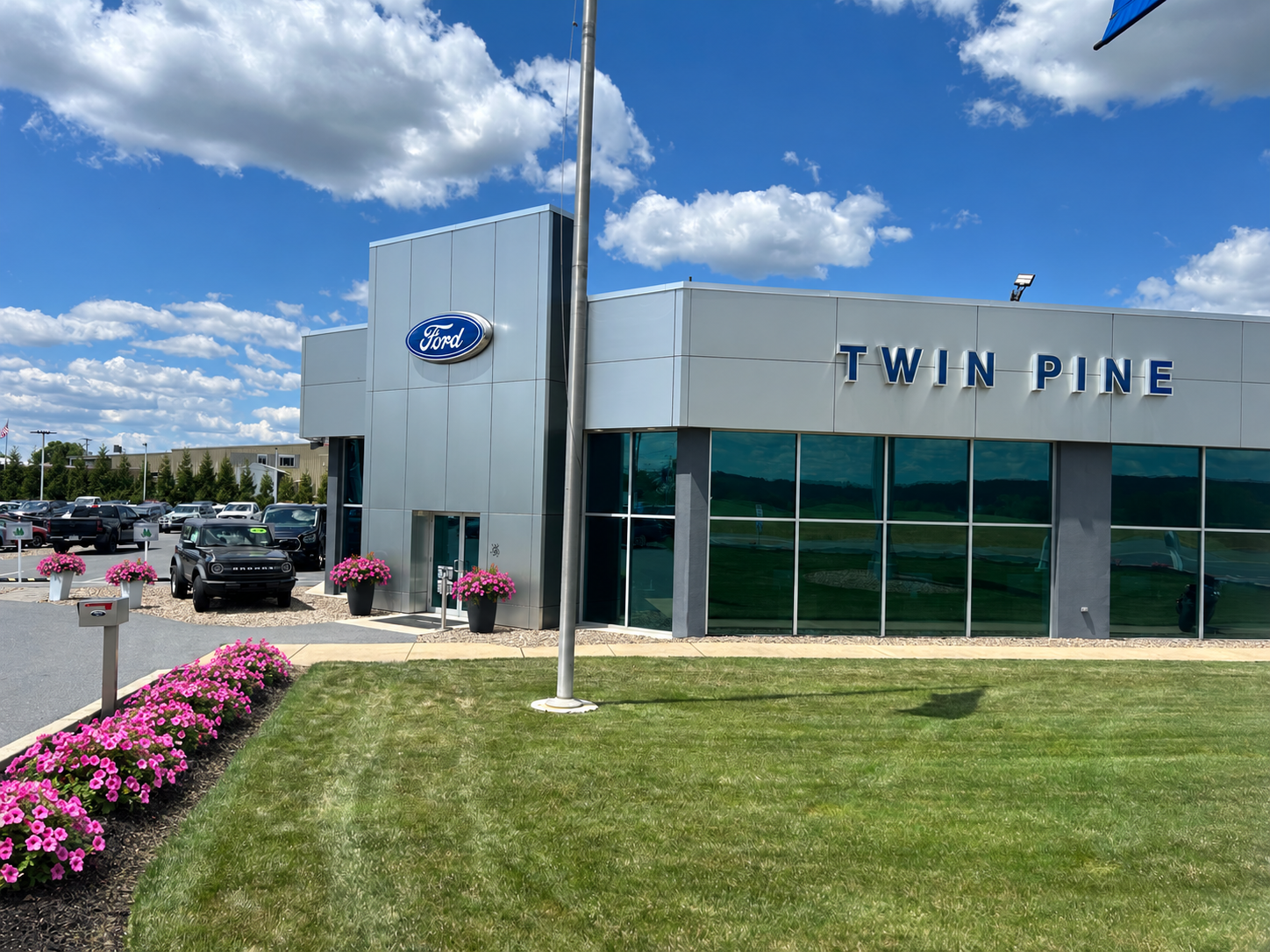 Exterior view of Twin Pine Ford dealership building with pink flowers on the lawn under a blue sky.