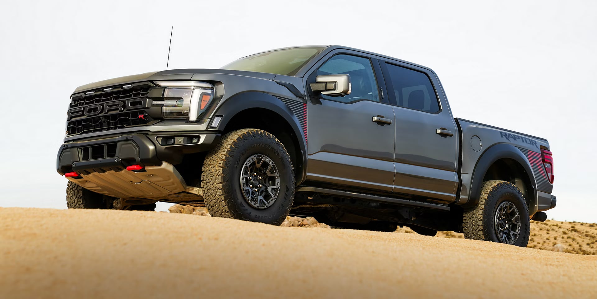 Low-angle view of a dark gray Ford F-150 Raptor R pickup truck parked on a sandy desert hill.
