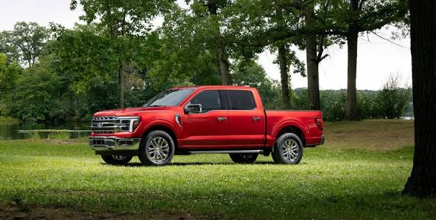 Red Ford F-150 SuperCrew pickup truck parked on green lawn surrounded by trees near a pond.