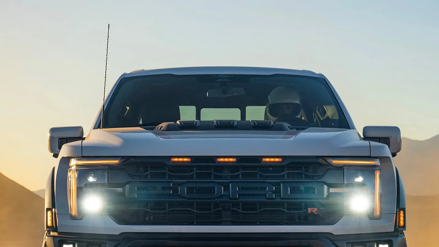Front view of a white Ford F-150 Raptor R truck with headlights on in the desert.