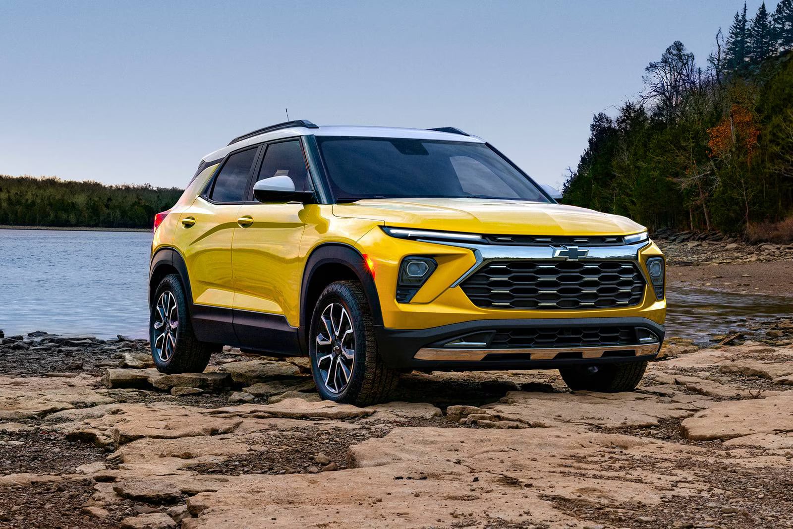Yellow Chevrolet Trailblazer with a white roof parked on a rocky lake shore.