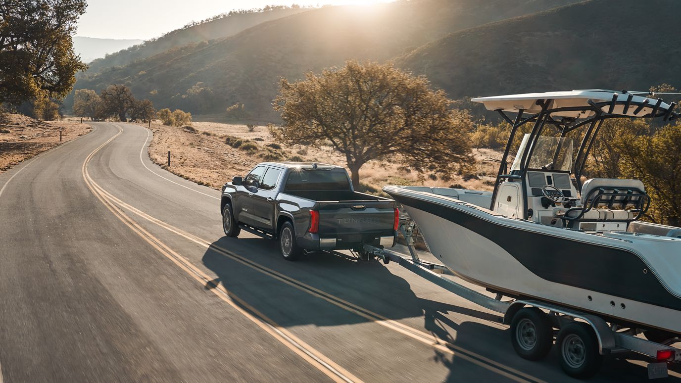 A grey Toyota Tundra towing a boat through a desert road.