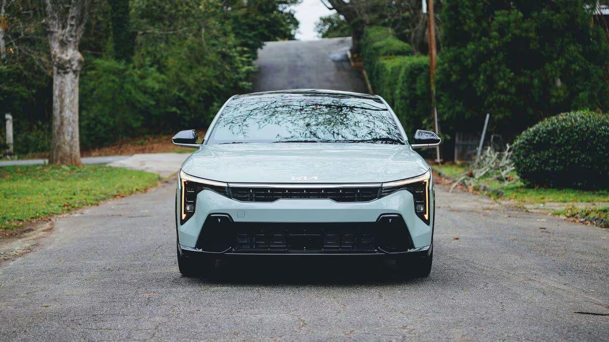 Front view of a light green Kia K4 parked on a tree-lined road.