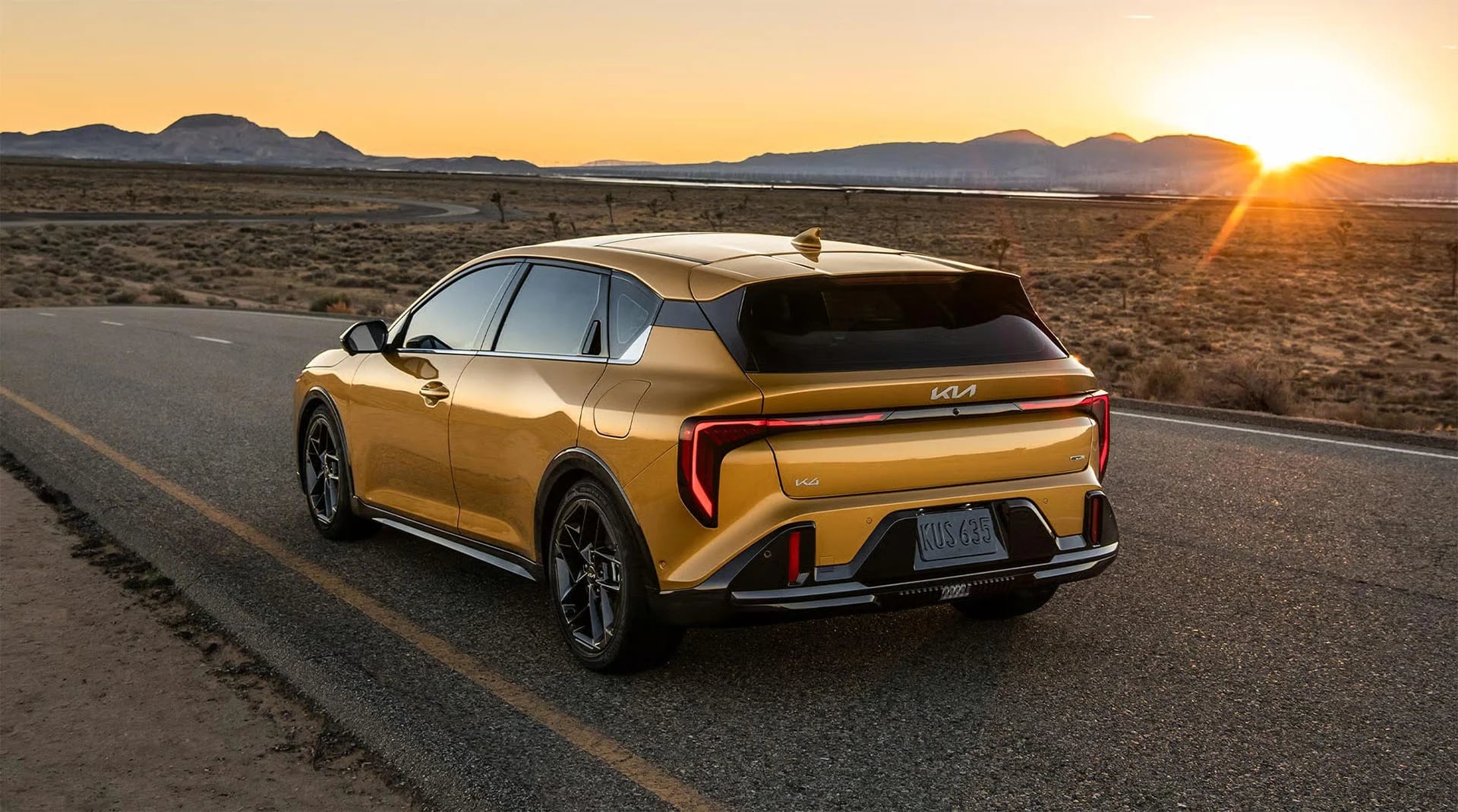 Gold 2026 Kia K4 Hatchback driving on a desert road at sunset.