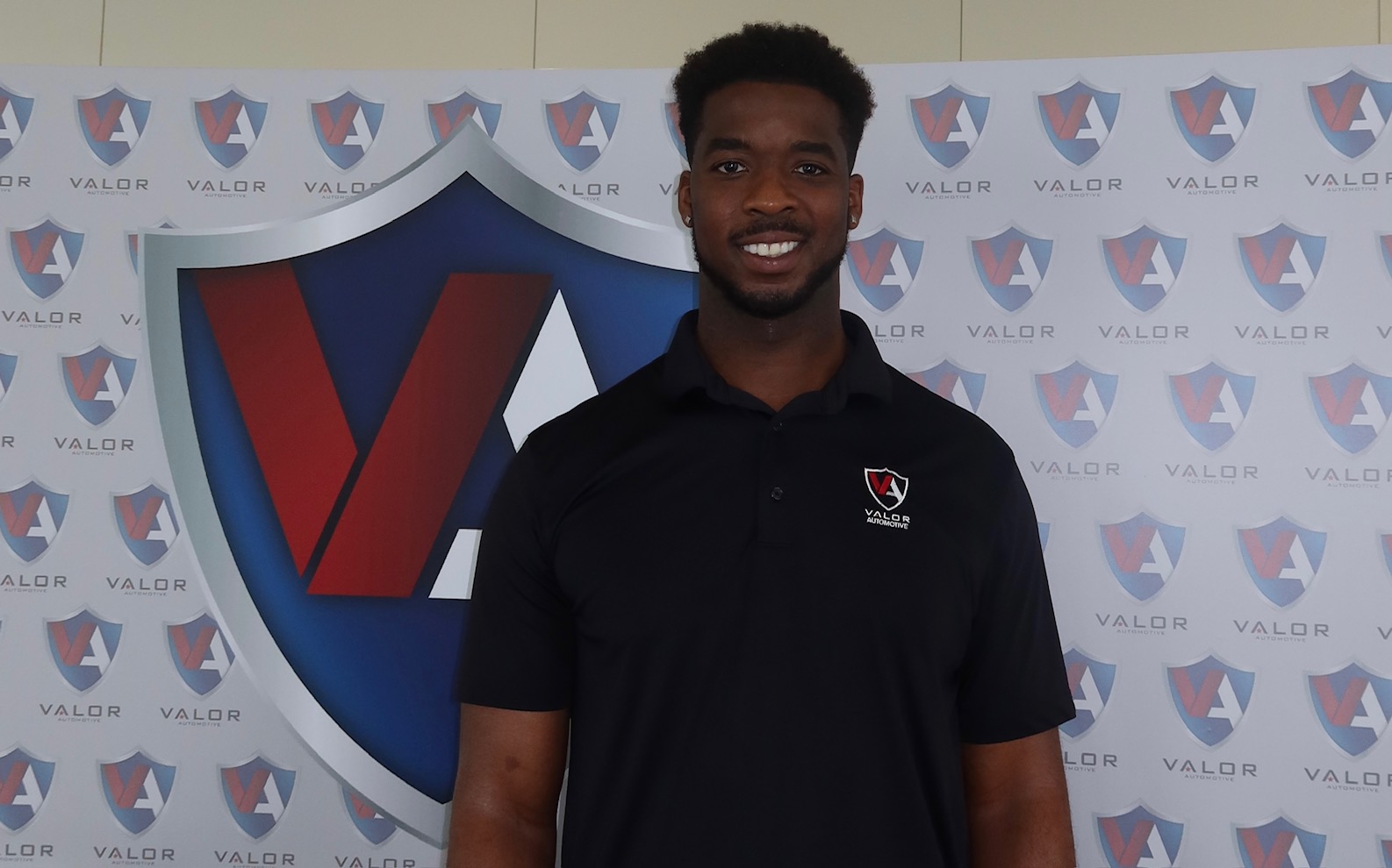 A smiling man wearing a black polo shirt stands in front of a Valor Automotive backdrop.