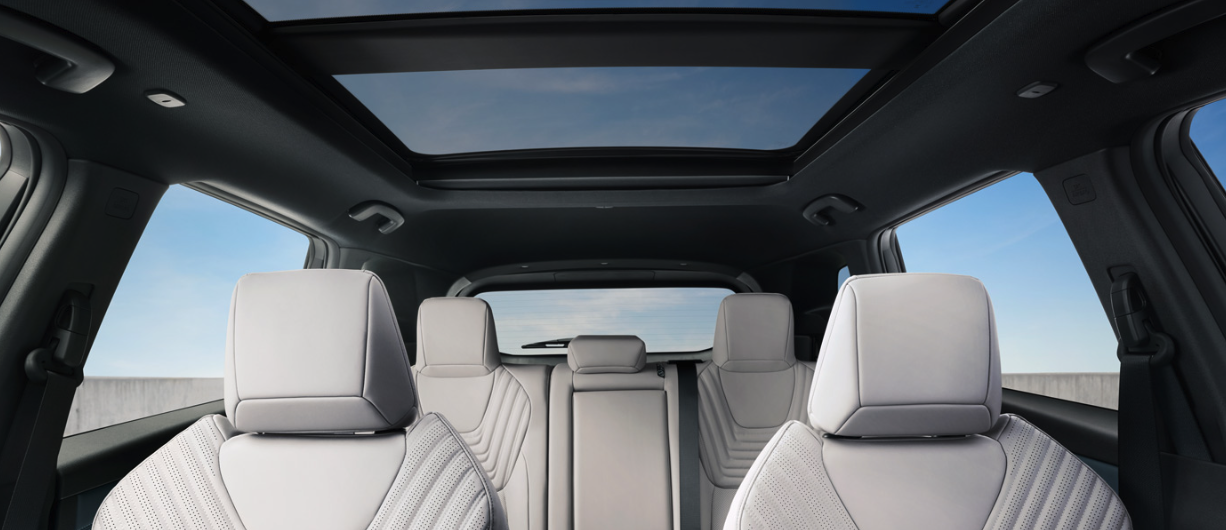 Front and rear view of modern car interior featuring light grey leather seats and a large panoramic glass sunroof.