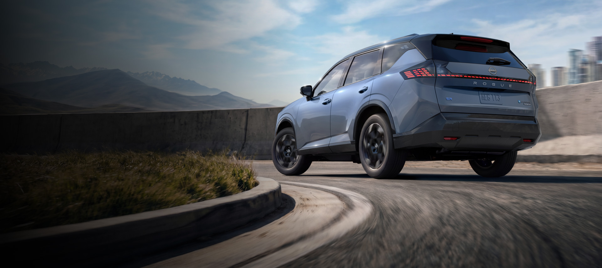 Rear view of a light blue Nissan Rogue driving along a winding mountain road under a bright sky.