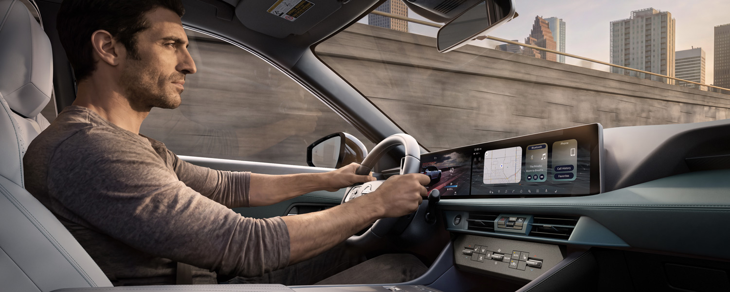 Driver holding steering wheel inside a modern car featuring a wide digital touchscreen and city backdrop.