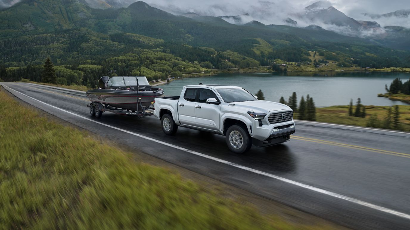 A silver Toyota Tacoma hauling a boat by a lake