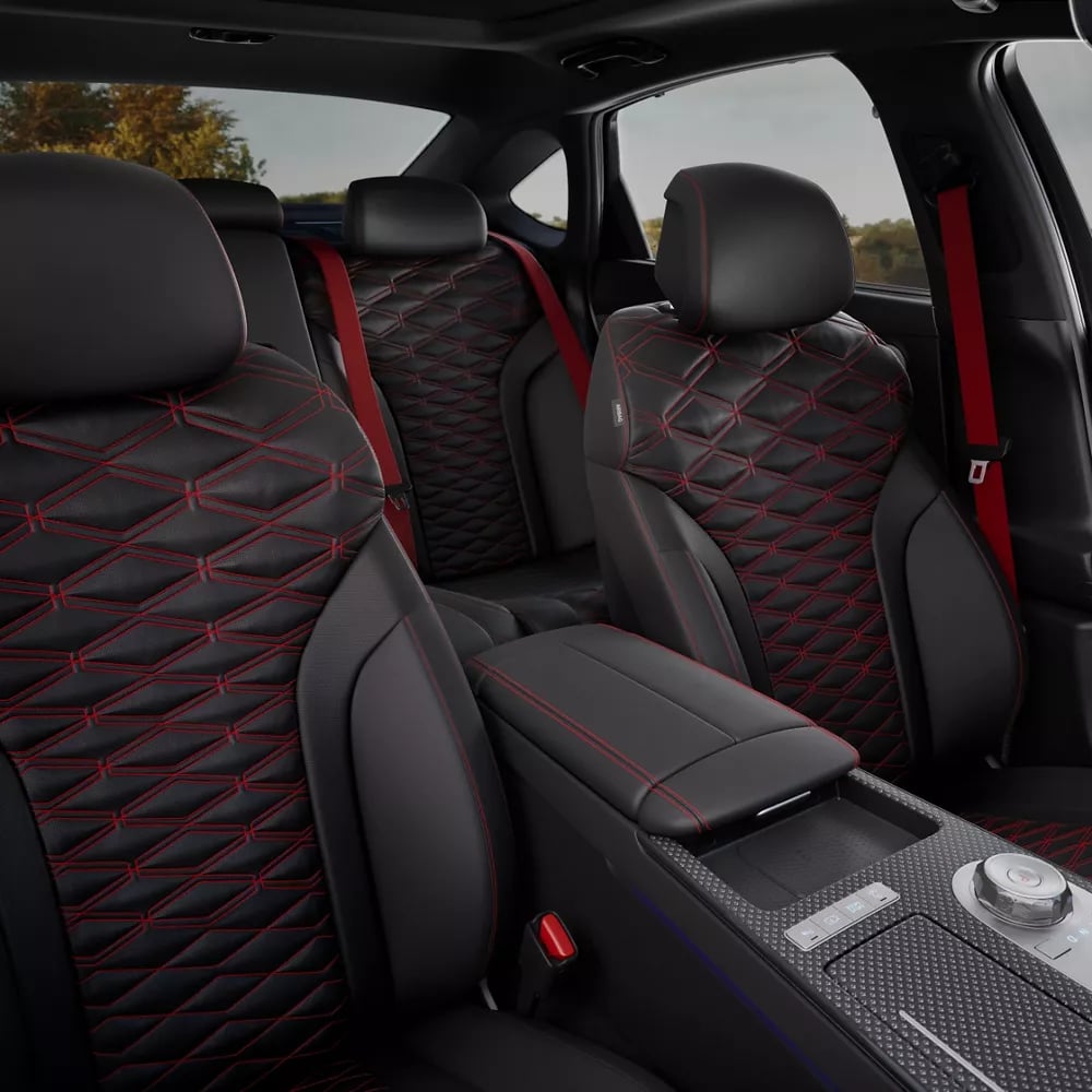 Black leather sports car interior with red diamond stitching on seats and vibrant red seatbelts.