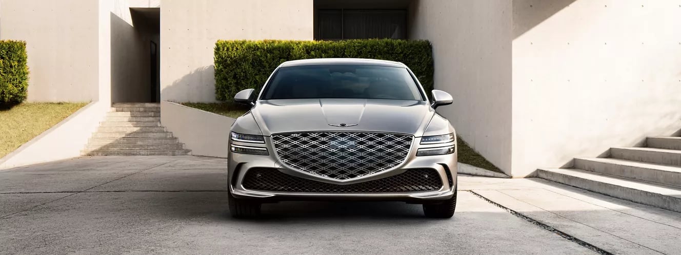 Front view of a sleek silver Genesis luxury sedan parked in front of modern concrete architecture.