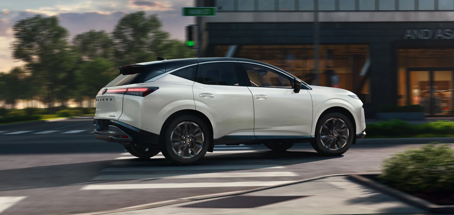 Side rear view of a white Nissan Murano with a black roof driving through a city intersection.
