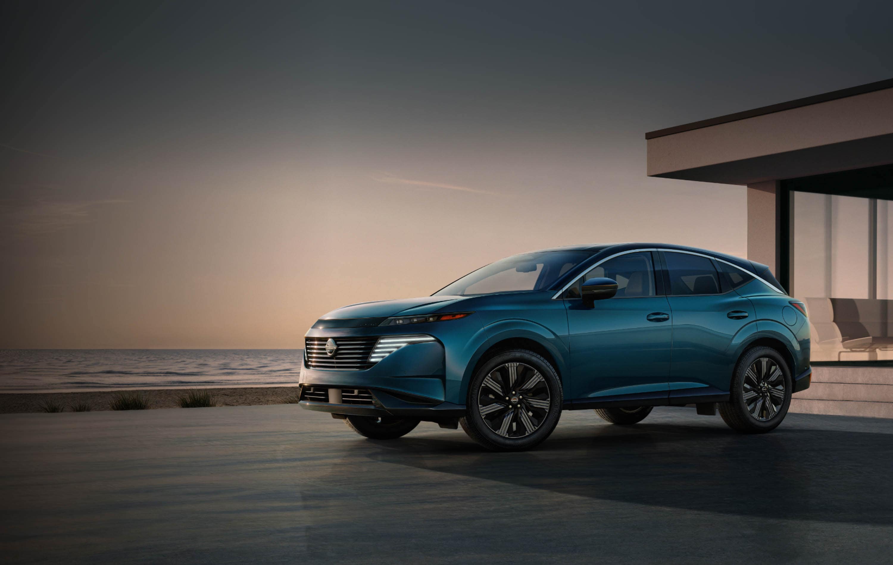 A dark teal Nissan SUV parked on a patio in front of a modern glass house overlooking the ocean at sunset.