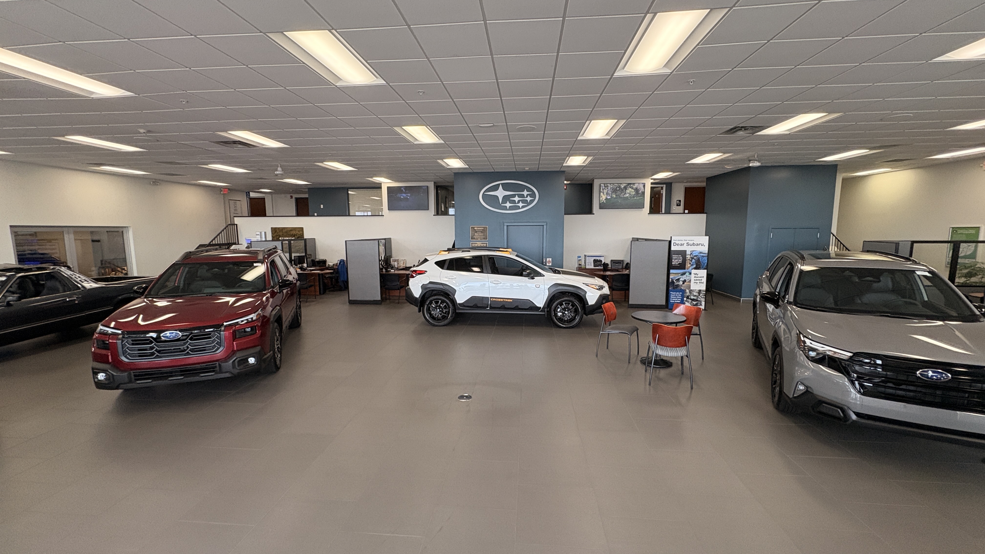 Subaru dealership showroom displaying red, white, and silver SUVs on a spacious tiled floor under bright ceiling lights.