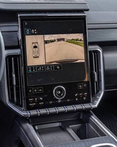 Vertical infotainment touchscreen in a car dashboard displaying surround-view camera feeds and climate controls.