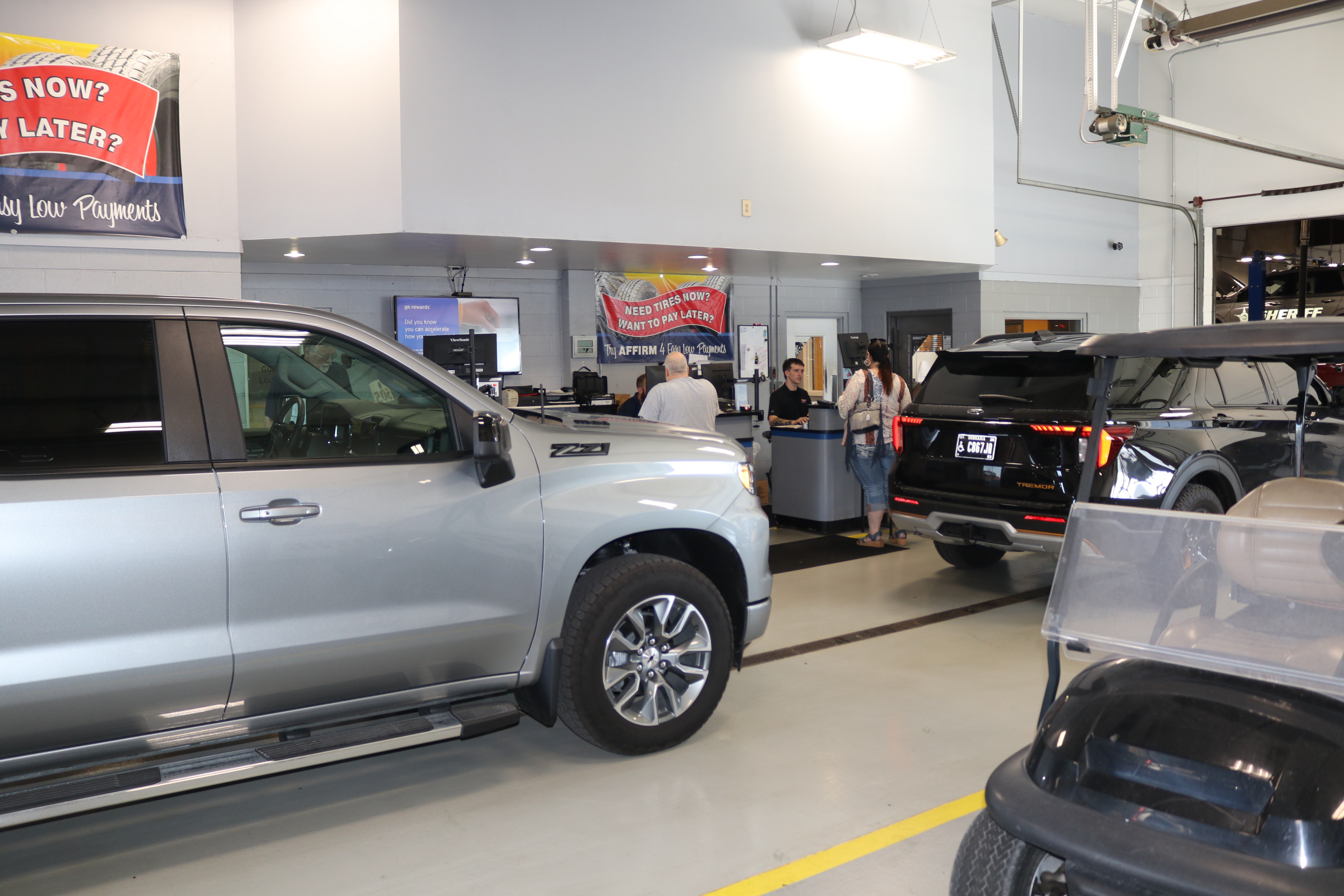 A silver Chevrolet pickup truck and a black SUV parked inside an auto service shop reception area.