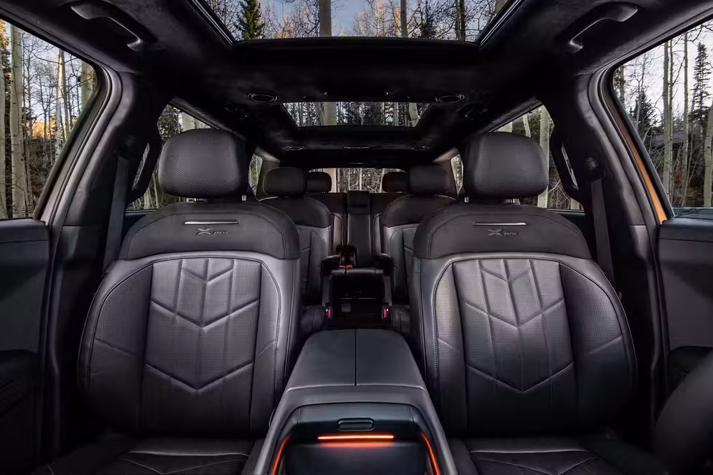 Luxurious black leather interior of a multi-row SUV with a dual-pane sunroof showing a forest background.