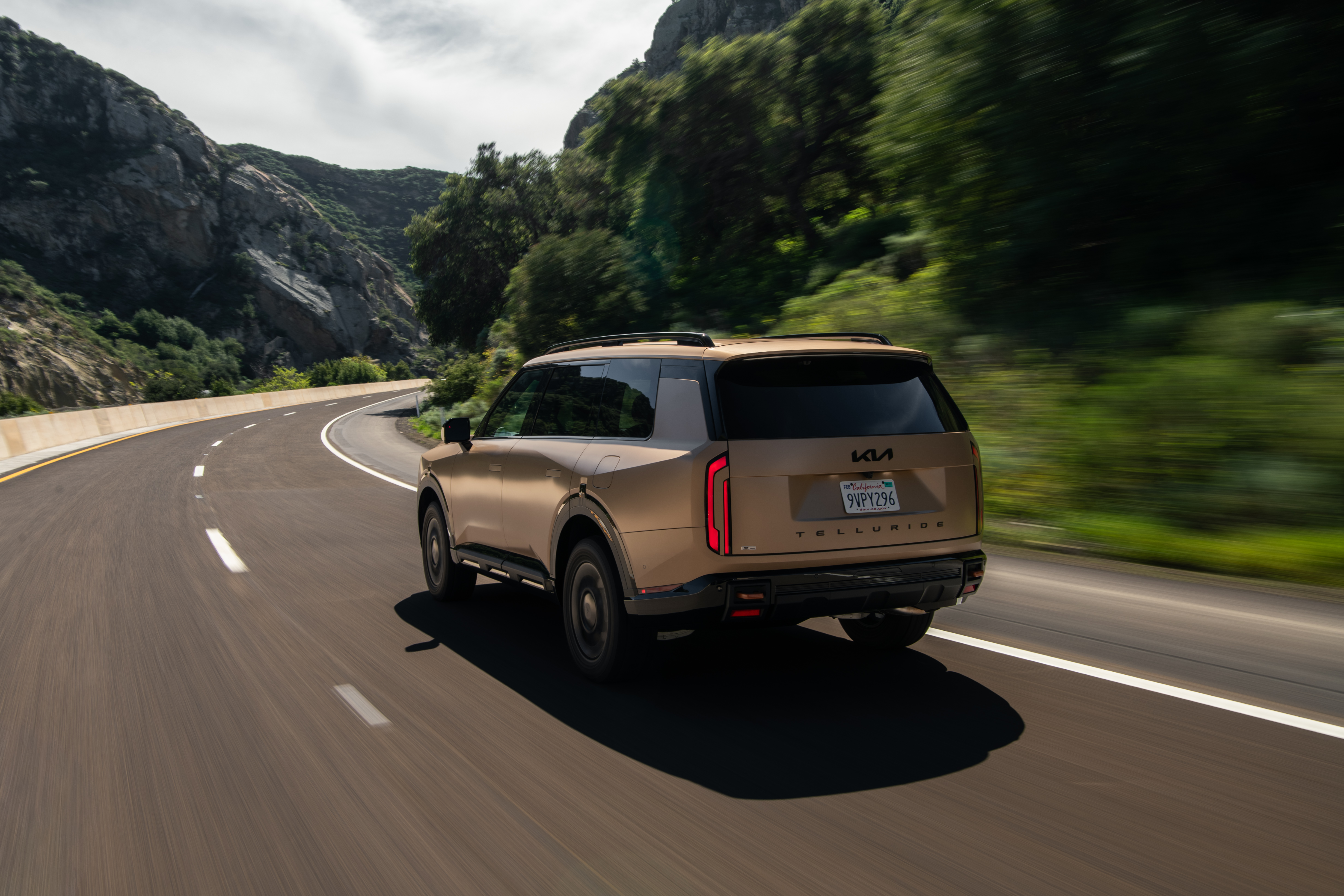 Rear view of a bronze Kia Telluride driving on a winding mountain road.