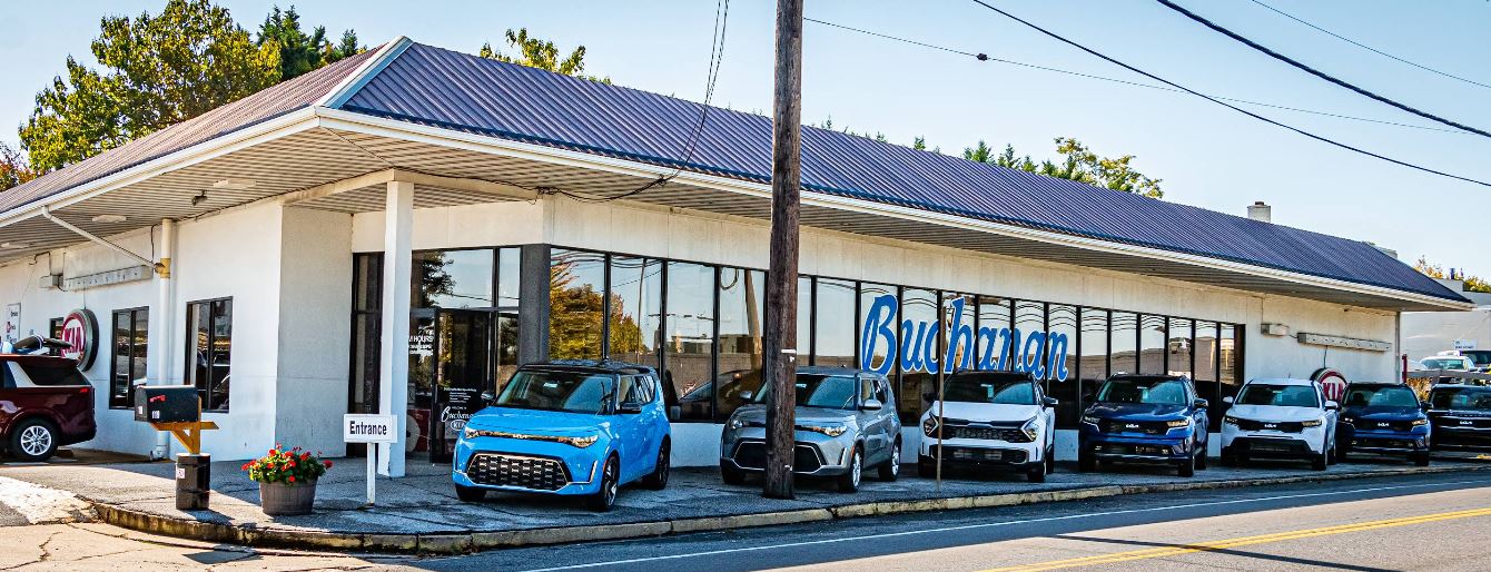 Line of new Kia SUVs parked in front of Buchanan Kia dealership showroom.