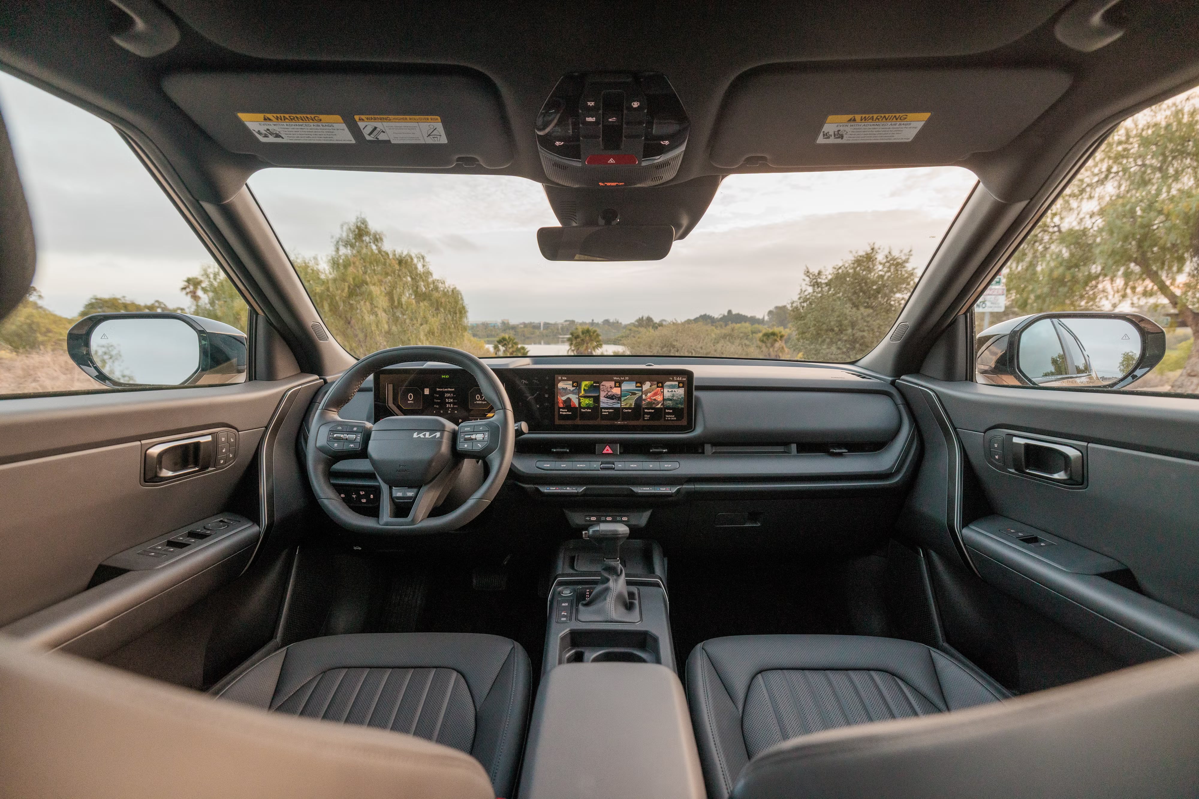 Interior view of a modern Kia dashboard, steering wheel, digital screen, and front leather seats.