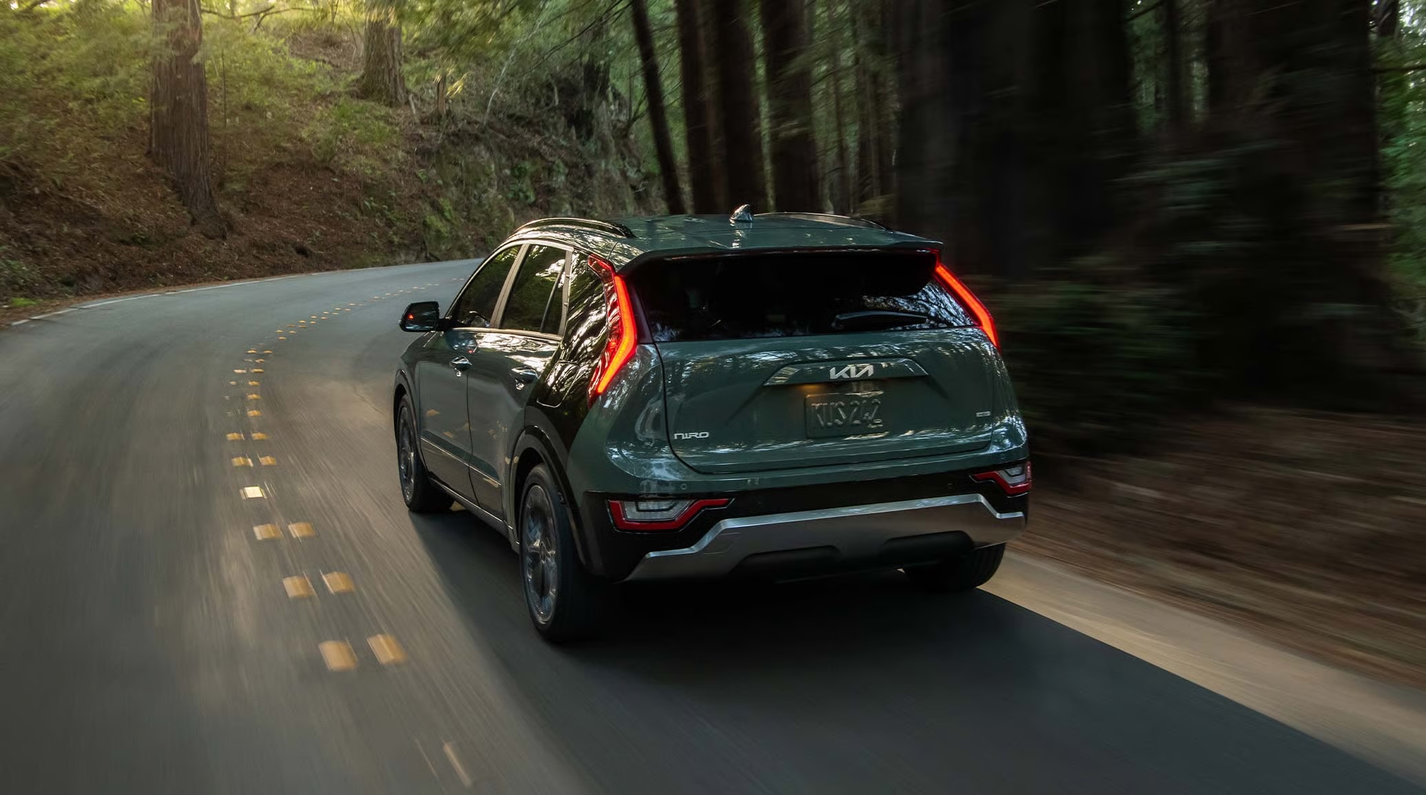 Dark green Kia Niro driving along a curved asphalt road through a dense forest.