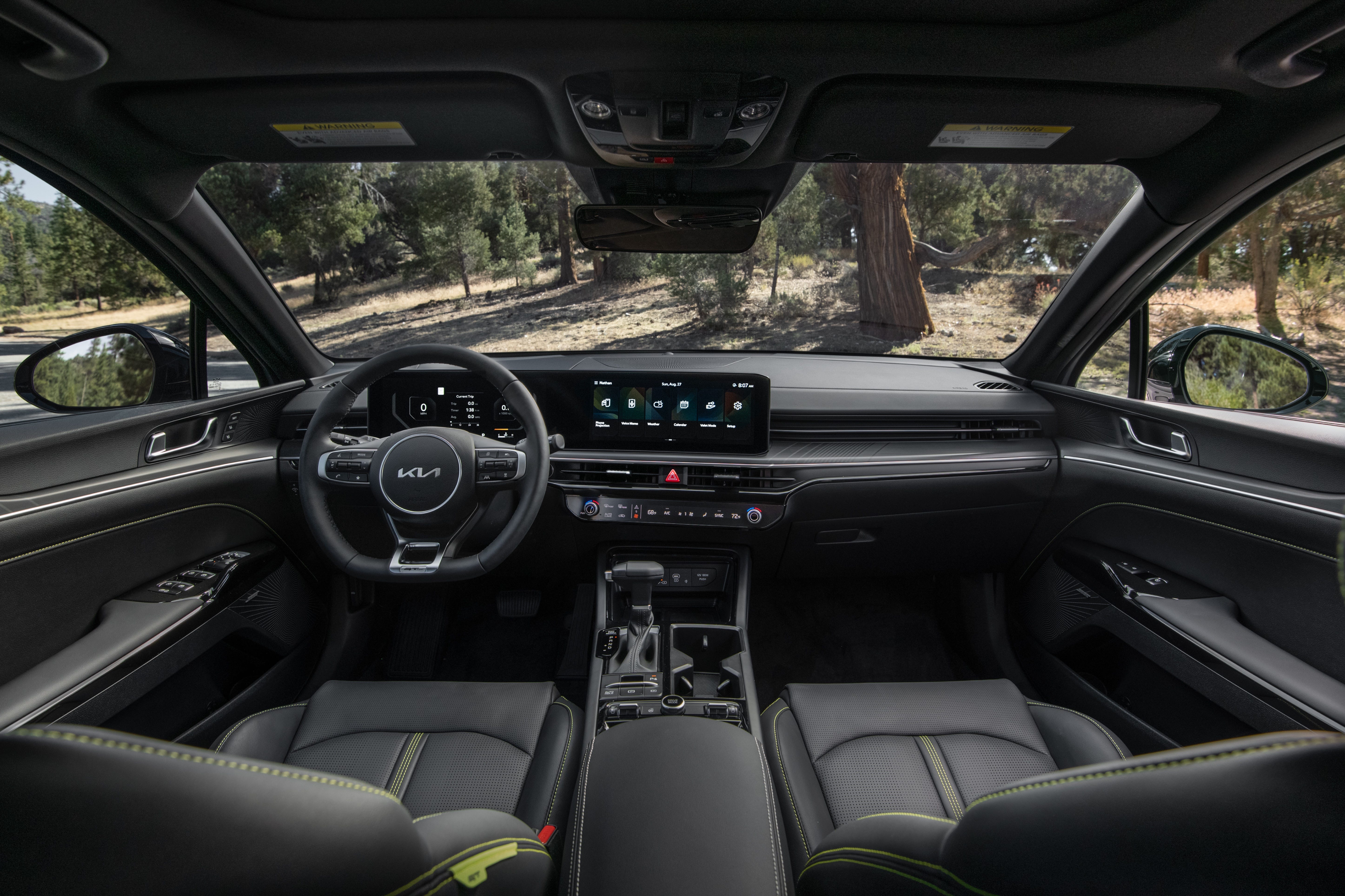 Dashboard and front seats inside a modern Kia featuring black leather upholstery and dual digital screens.