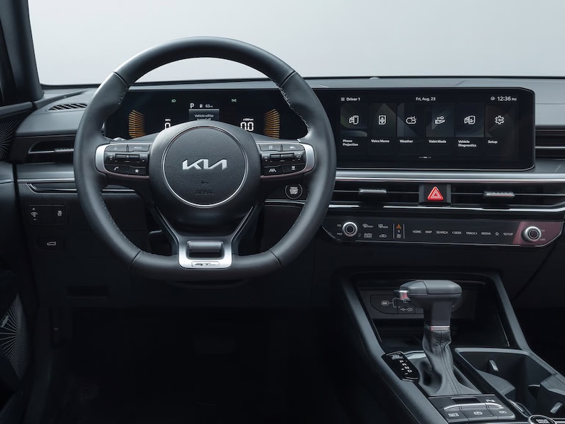Driver-side view of a modern Kia GT-Line interior featuring a leather steering wheel, digital cluster, and touchscreen.