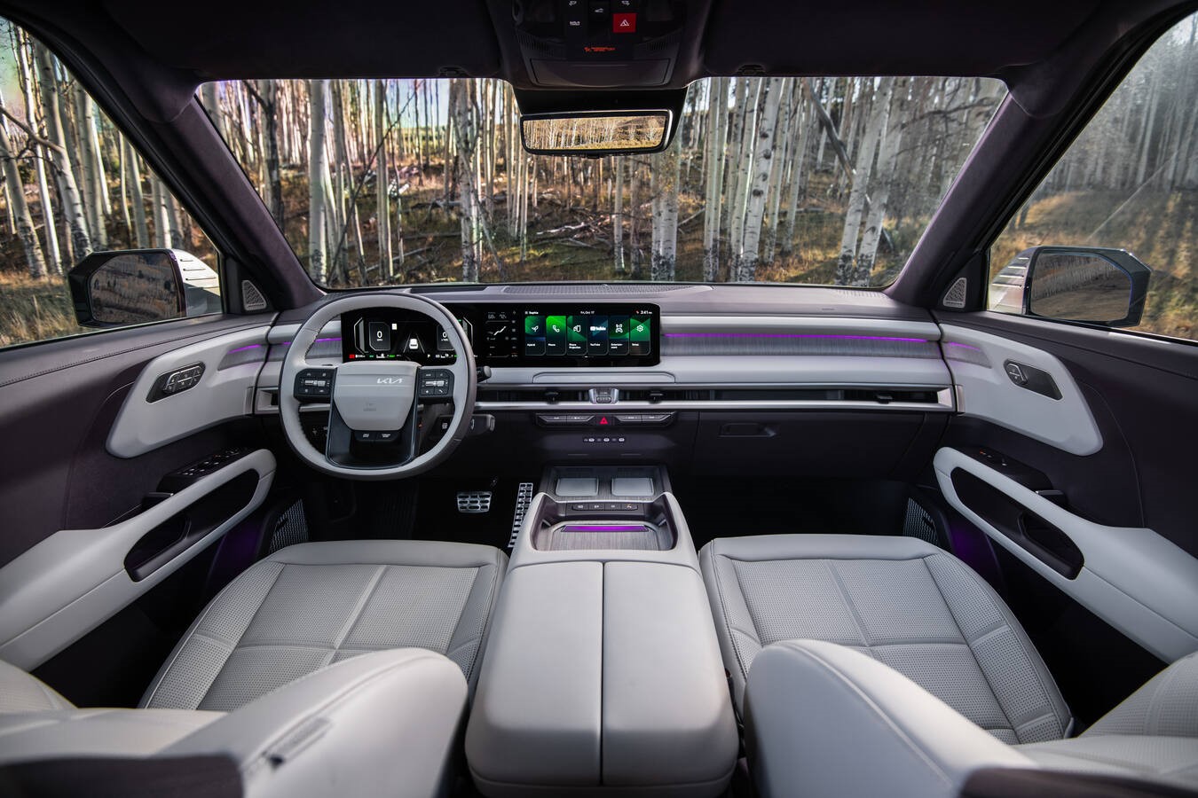 Light gray interior of a modern Kia EV with dual dashboard displays and a forest view through the windshield.