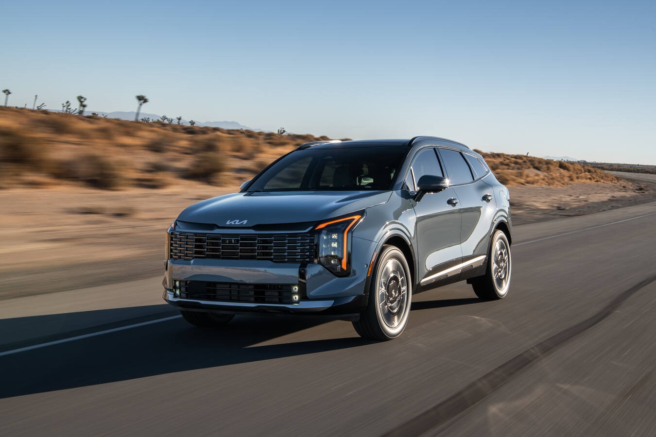 A blue-gray Kia Sportage driving along a desert highway.