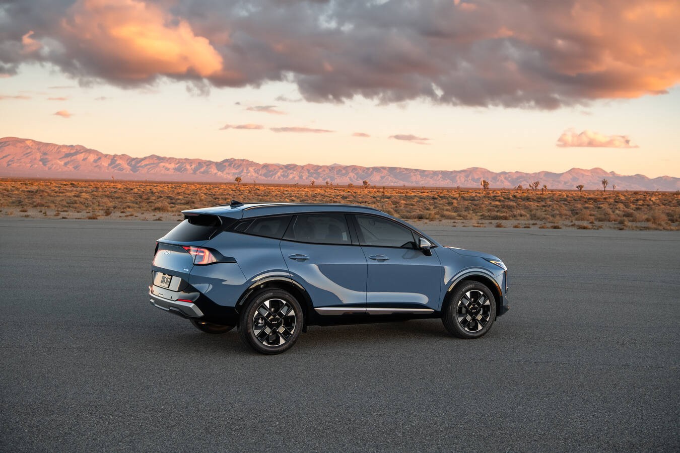 Slate blue Kia Sportage parked with mountains in the background.
