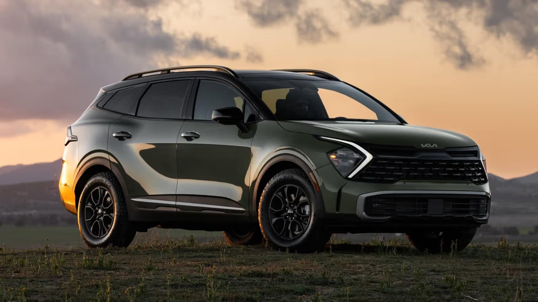 Dark green Kia Sportage parked on a grassy hill at sunset.