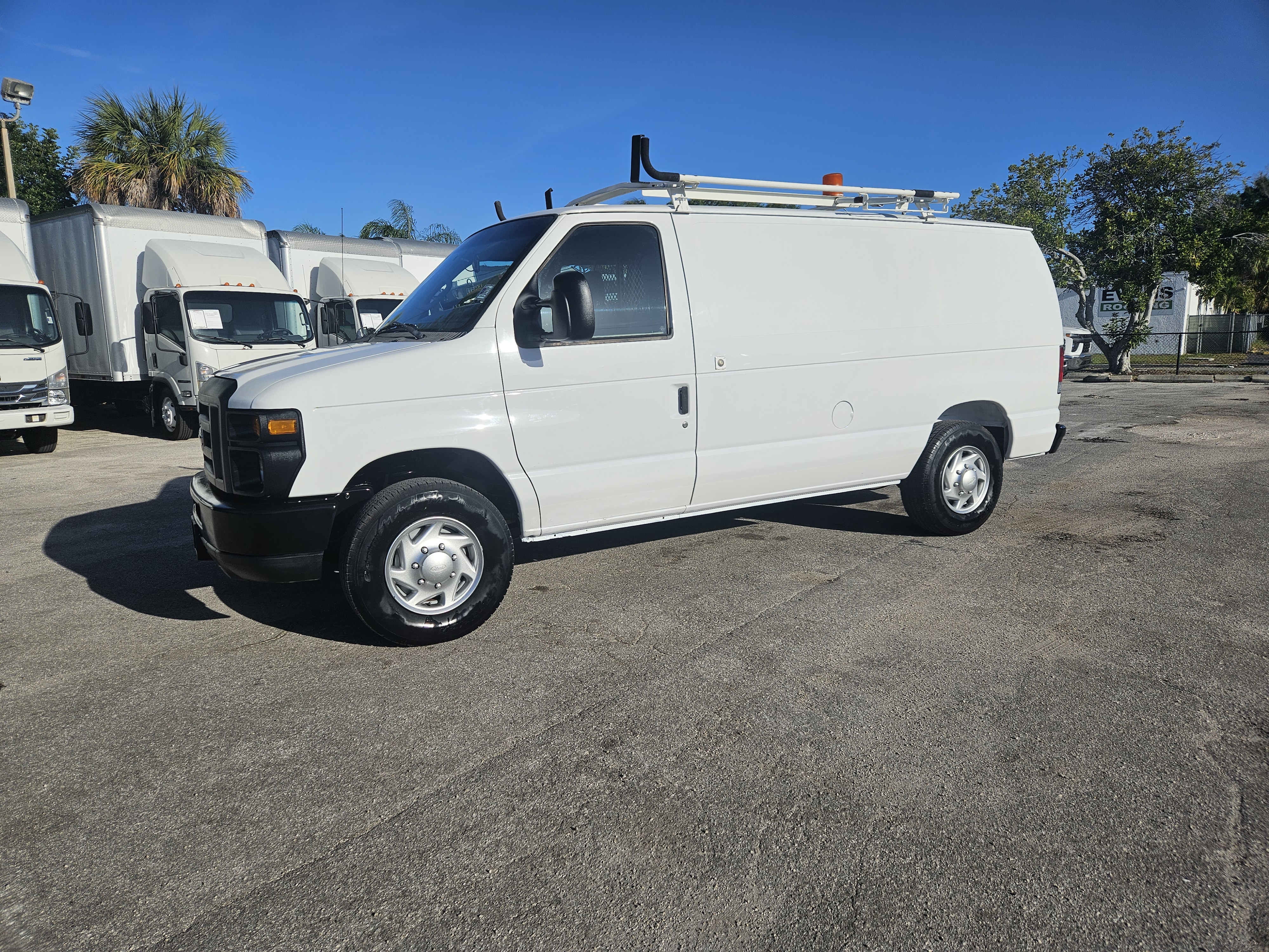 White Ford Econoline cargo van with roof rack parked on asphalt.
