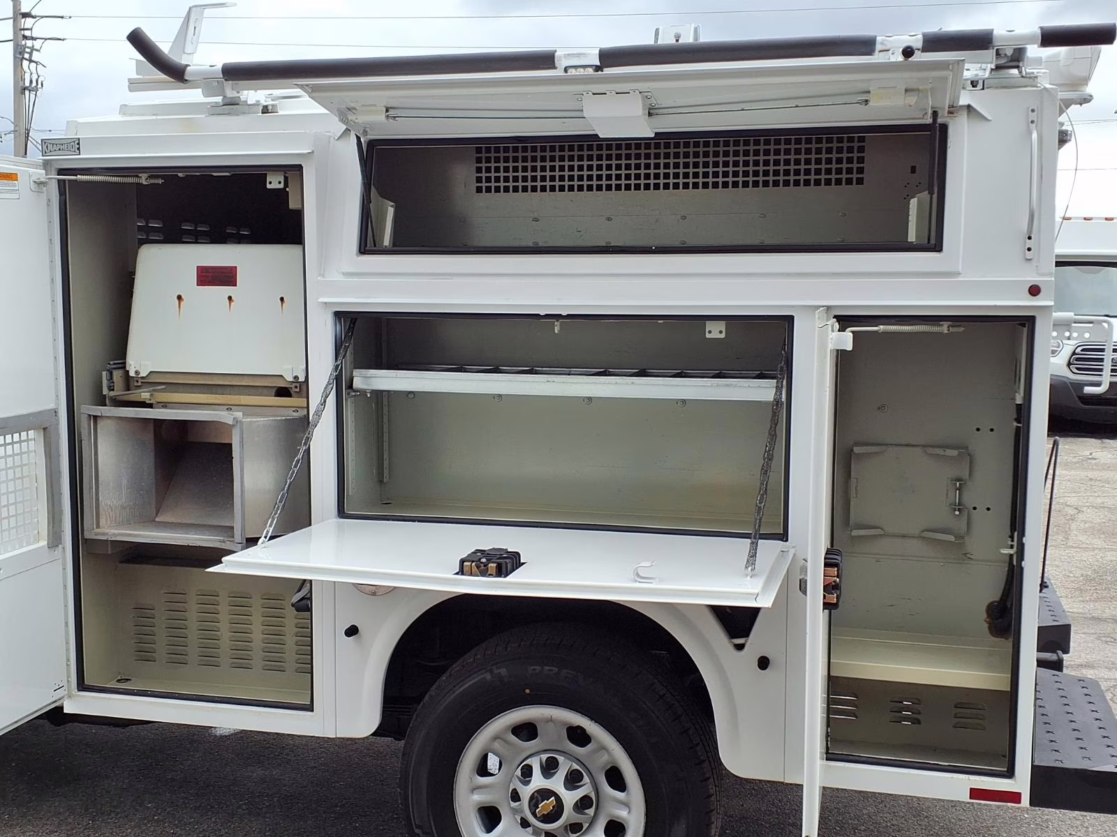 Side view of a white service body truck with all compartments open, showing drawers, shelving, and specialized tool storage hooks.