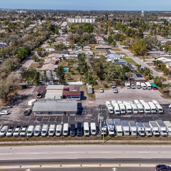 Aerial view of a commercial vehicle lot with many white box trucks and vans parked next to a residential neighborhood.
