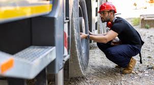 A technician checking the tread depth and brake pads on a heavy-duty box truck tire.