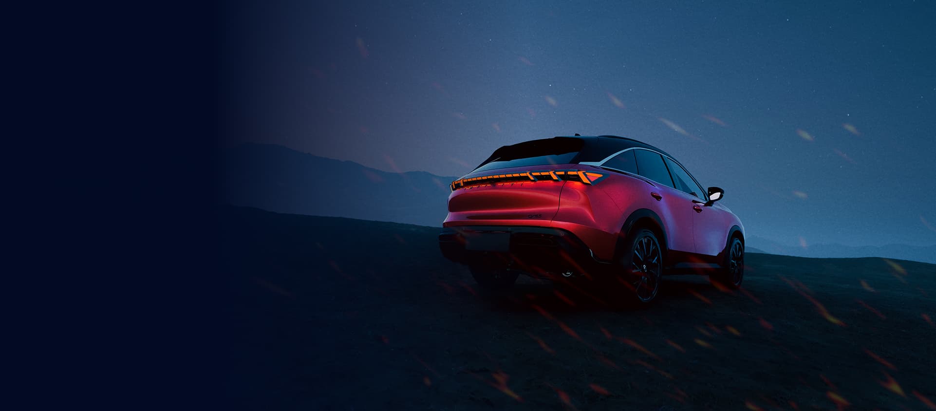 Red electric SUV parked on a dark hillside under a starry night sky with glowing embers.