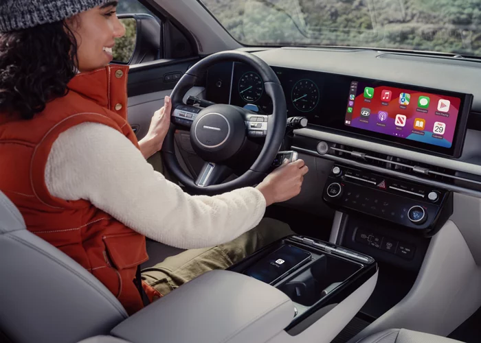 Woman sitting in a car driver's seat using a large touchscreen display with smartphone integration.